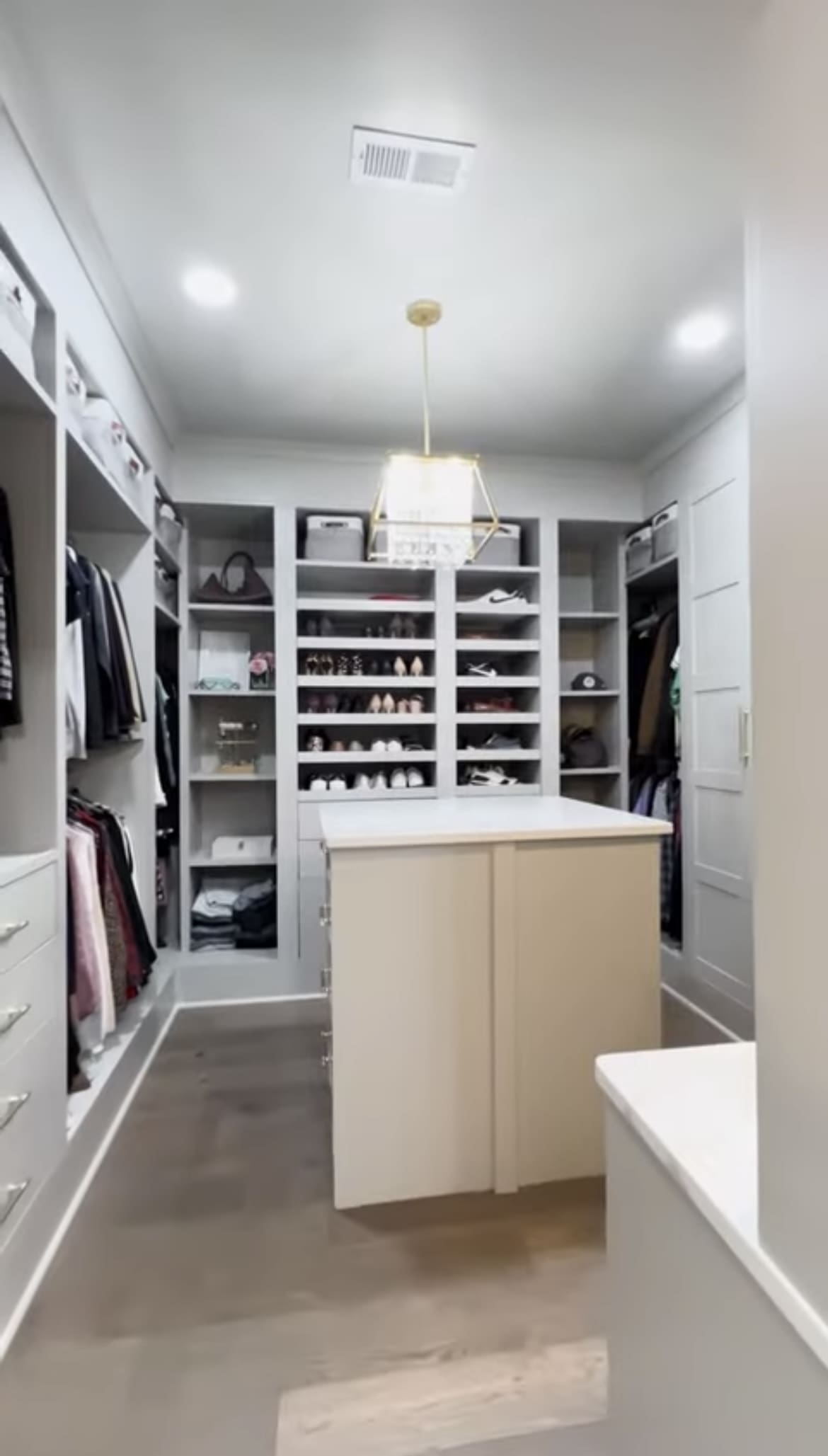 A large walk in closet with white cabinets and shelves.